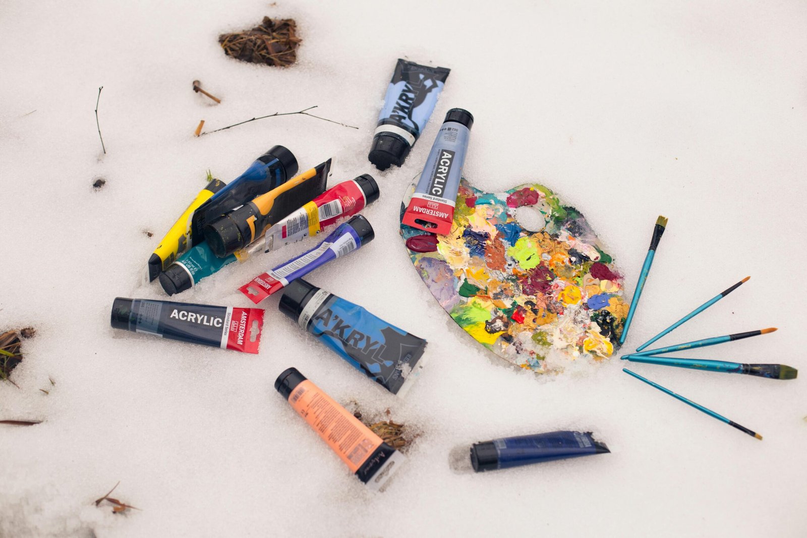 Home Colorful acrylic paint tubes and palette with brushes lying on a snow surface, artistic winter theme.